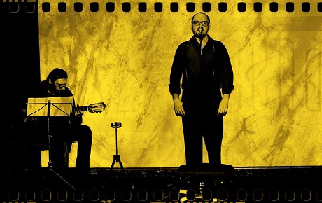 Na żółtym tle po lewej mężczyzna gra na gitarze, po prawej mężczyzna stoi przy mikrofonie , śpiewa.