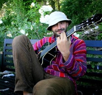 Na zdjęciu młody mężczyzna w kapeluszu, gra na gitarze.