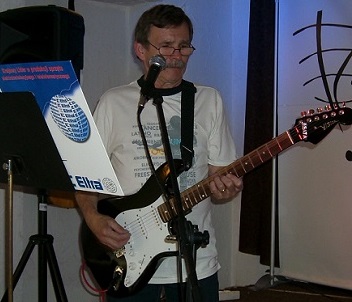Na zdjęciu szczupły mężczyzna w średnim wieku, w okularach, stoi na scenie, gra na gitarze elektrycznej