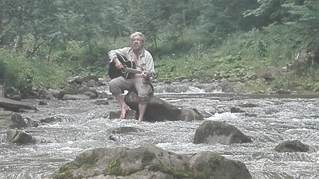 Mężczyzna z gitarą siedzi na kamieniu w górach.