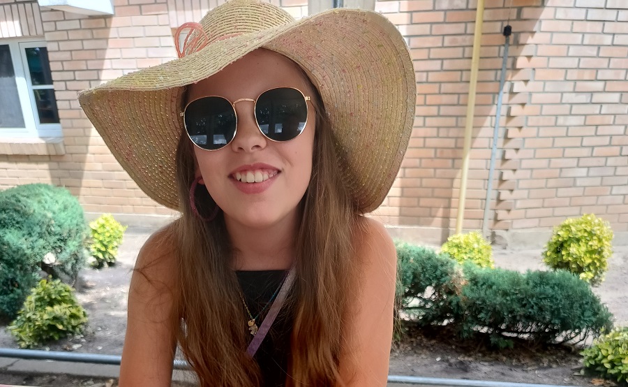 dziewczynka w okularach przecowsłonecznych i kapeluszu, uśmiecha się