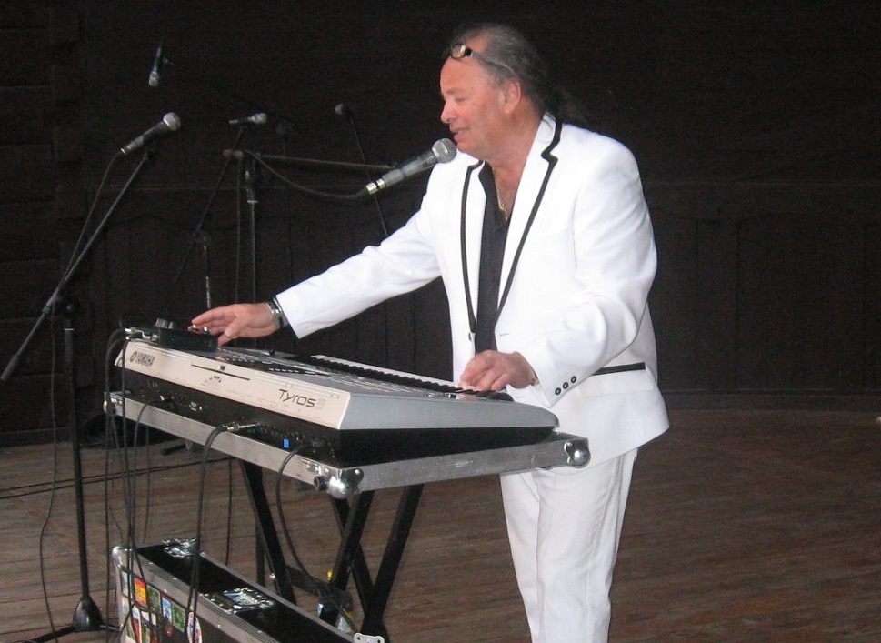 mężczyzna w średnim wieku w białym garniturze przy pianinie elktronicznym